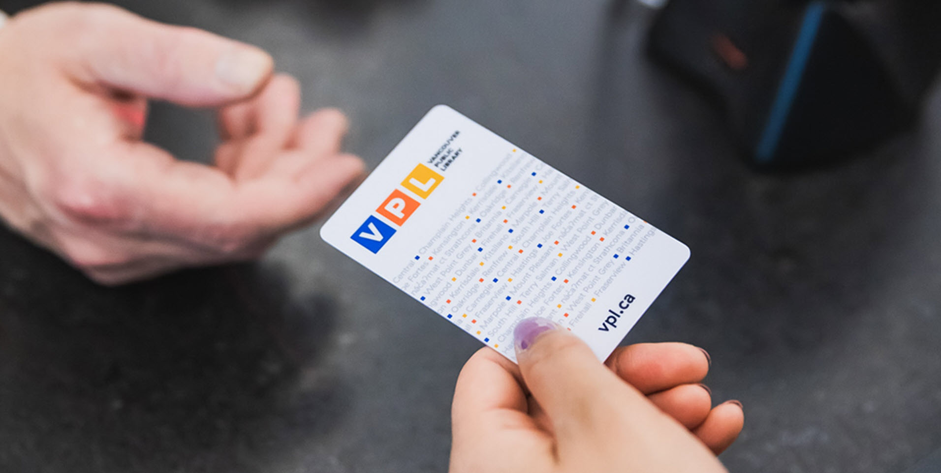 A photo of a person handing a Vancouver Public Library card to another person.