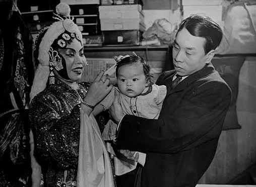 Archival photograph of Chinese opera performer, backstage, with man and baby