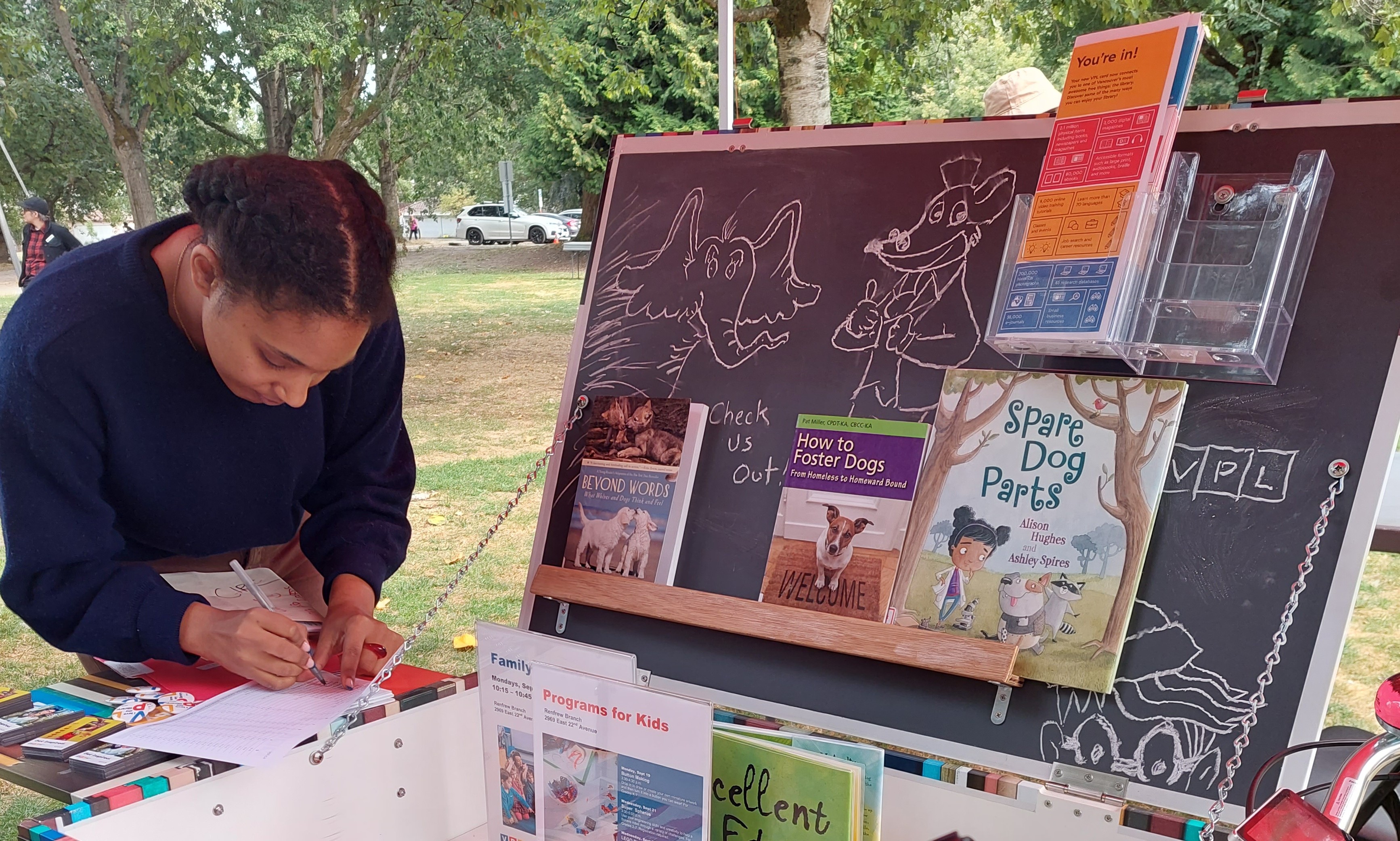 A photograph shows a person filling out a form at the BiblioBike during an outdoor event.