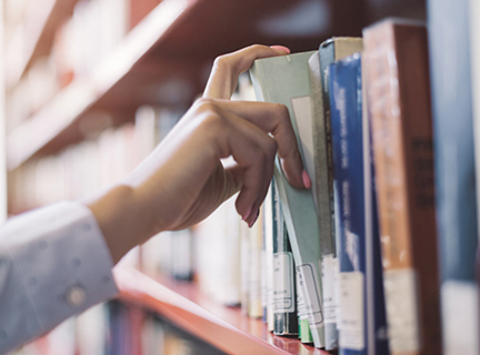 An extended hand picks a book from a library shelf