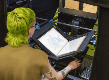 A person is using the Scribe digitization machine to scan a rare book