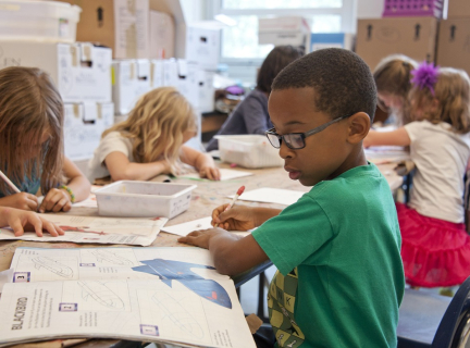 boy in green sweater writing on white paper