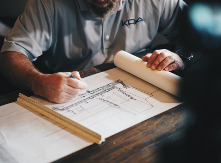 a man working on a schematic of a building, using a pen and a ruler.