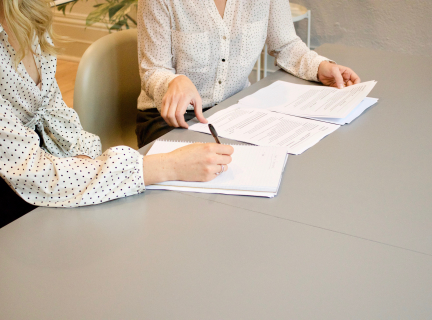 Two women seated at a table examining some paper documents.