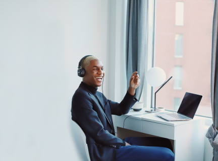 a man in a suit is seated at a desk with a laptop on it, he is wearing headphones, smiling and speaking.