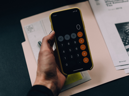 Photograph of a hand holding an iPhone with the Calculator app open above a file folder filled with mail and printouts.