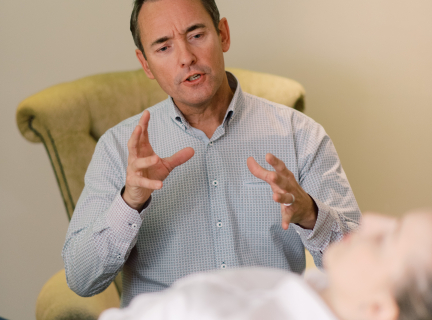 one seated person speaking to another person lying on their back in an office