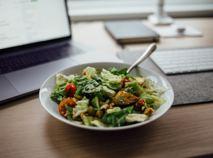 a bowl of salad next to a computer and notebook