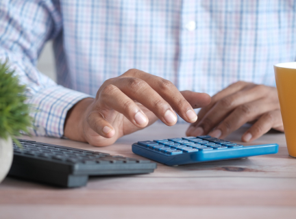 close-up of a man sitting at a desk by a computer, using a calculator