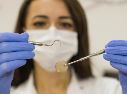 a dentist holds up a mouth mirror and a dental probe.