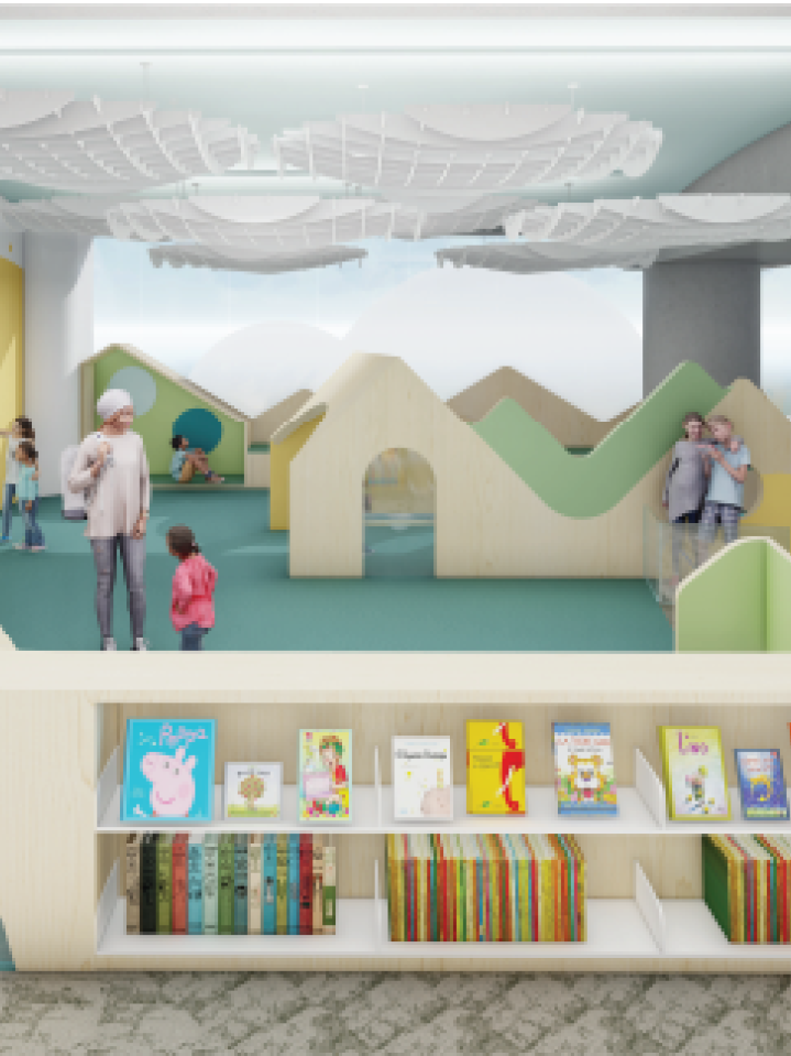 A computer rendering of a play space consisting of low hill-shaped dividers and cloud-shaped lighting on the ceiling, reminiscent of a stylized outdoor play area. In the foreground is a low bookshelf filled with children's books.