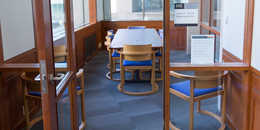 The Central Library L4 North meeting room looking through the door. There is one rectangular table surrounded by six chairs and three additional chairs facing away from the camera near the door.