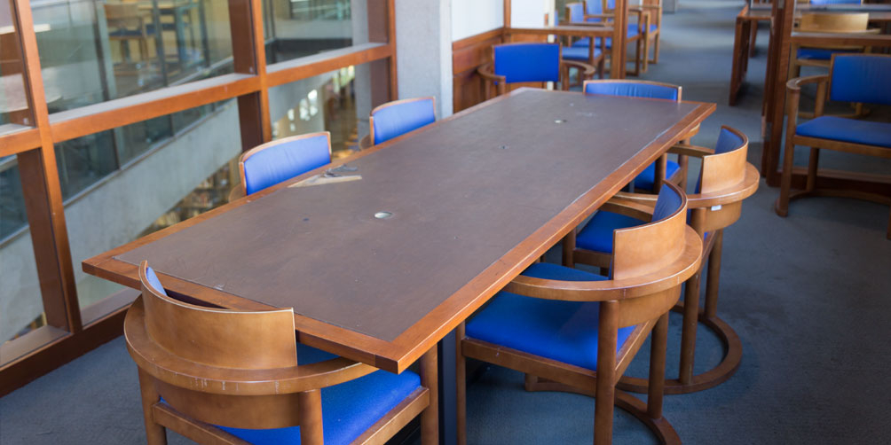 The Central Library L6 North meeting room towards the door. There is one rectangular table surrounded by six chairs and two additional chairs facing towards the camera on either side of the door.