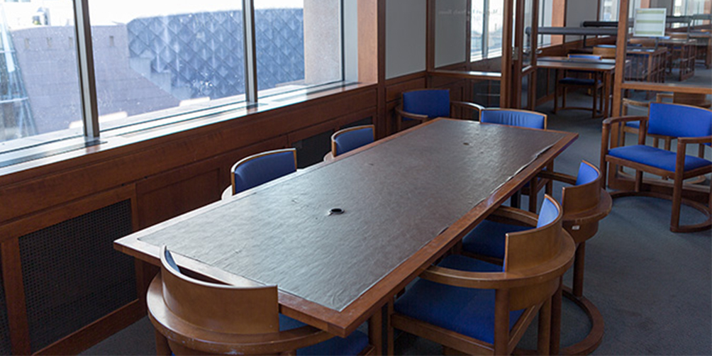 The Central Library L6 South meeting room looking towards the door. There is one rectangular table surrounded by six chairs and two additional chairs facing towards the camera on either side of the door.