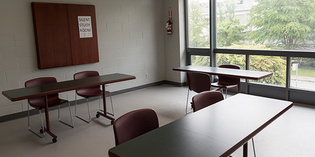 The Firehall meeting room looking toward the windowed back wall. There are three small tables, each with two chairs.