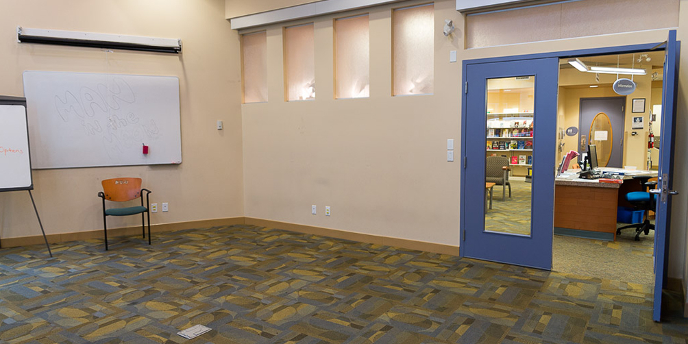 The Kensington meeting room looking toward the doors leading to the main library area. There is a whiteboard, a flipchart and a chair against the wall. 