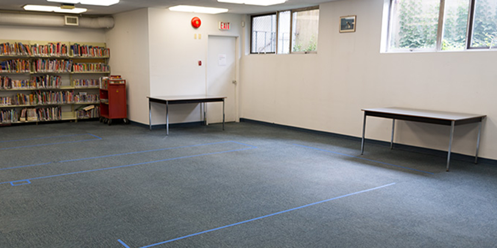 The Kitsilano meeting room looking toward the windowed back wall and the emergency exit. There are two small tables visible, and a portion of a bookshelf against the wall. 