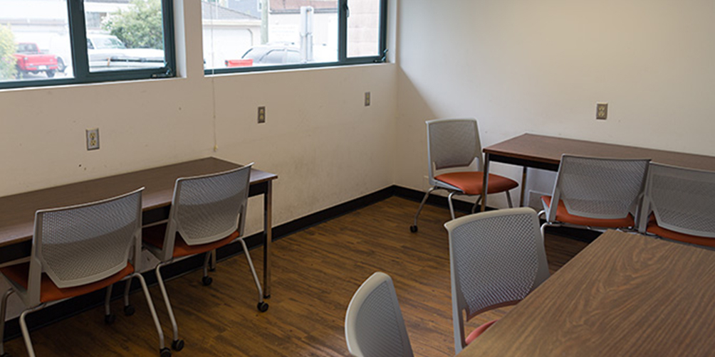 The South Hill meeting room looking toward the windowed back wall. There are three small tables, each with two or three chairs.