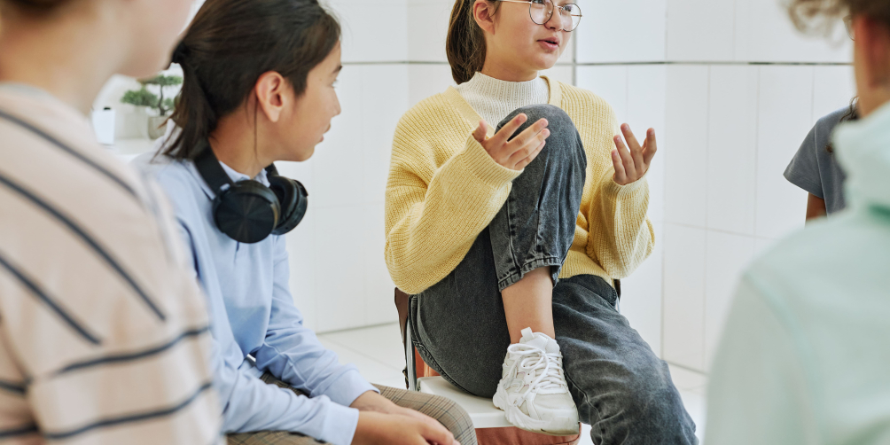 A group of teens sit in a circle and converse.