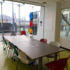 Photograph of Nellie Yip Quong room with tables and chairs set up at the center of a brightly lit room against the backdrop of the city street on the other side of the floor to ceiling window