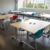 A large room with six tables and four colourful plastic chair around each table.